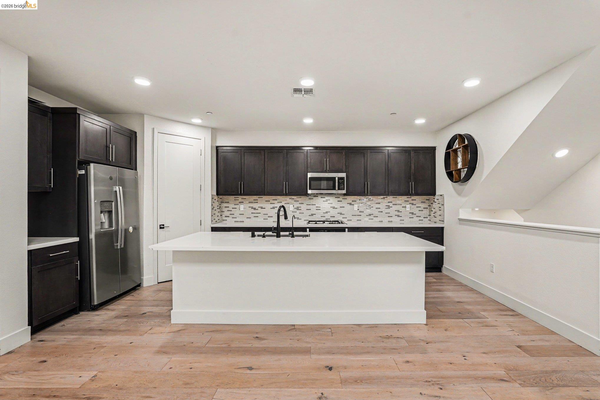 18210 Argento Loop San Ramon, CA 94583 - Photo 12 of 43 Kitchen featuring a central island with a sink, dark wood cabinetry, stainless steel appliances, light wood-finish flooring, and recessed lighting