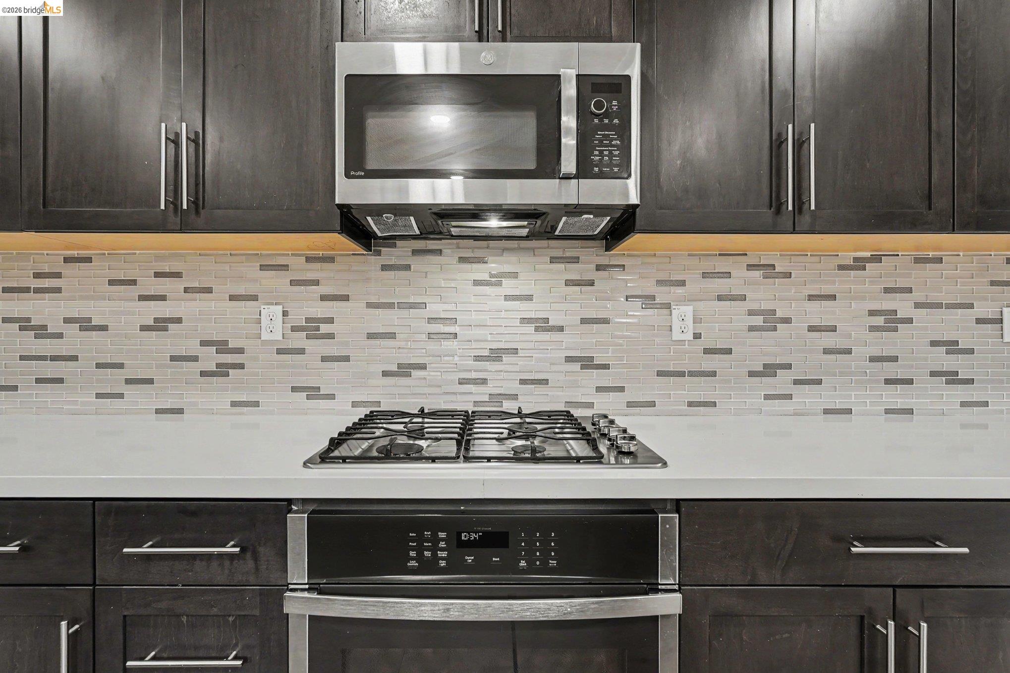 18210 Argento Loop San Ramon, CA 94583 - Photo 14 of 43 Kitchen featuring dark wood-finish cabinetry, stainless steel microwave, gas cooktop, built-in oven, and a mosaic tile backsplash