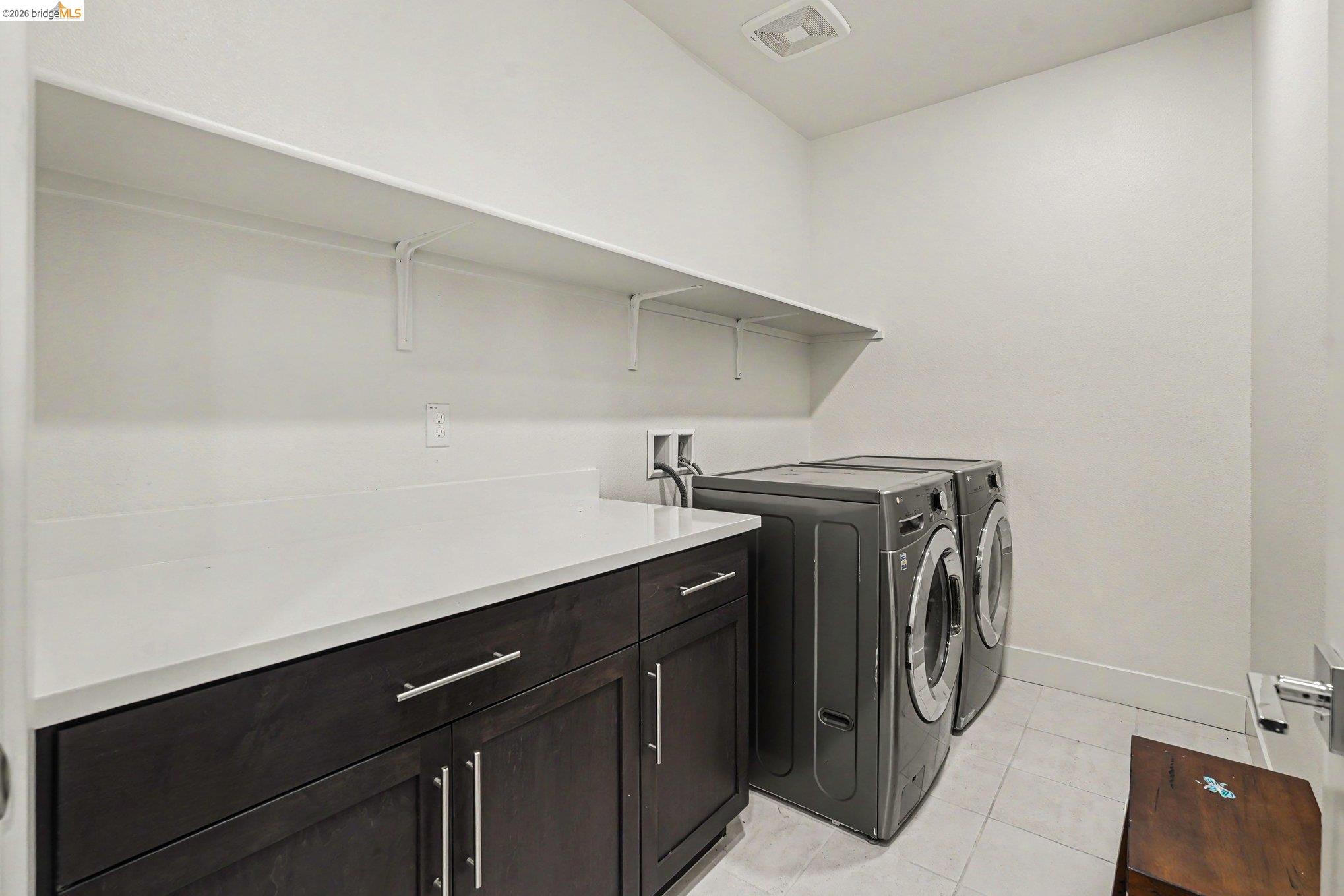 18210 Argento Loop San Ramon, CA 94583 - Photo 16 of 43 Functional laundry area featuring dark wood-finish cabinetry with silver hardware, a light-toned countertop, and an open wall shelf for storage