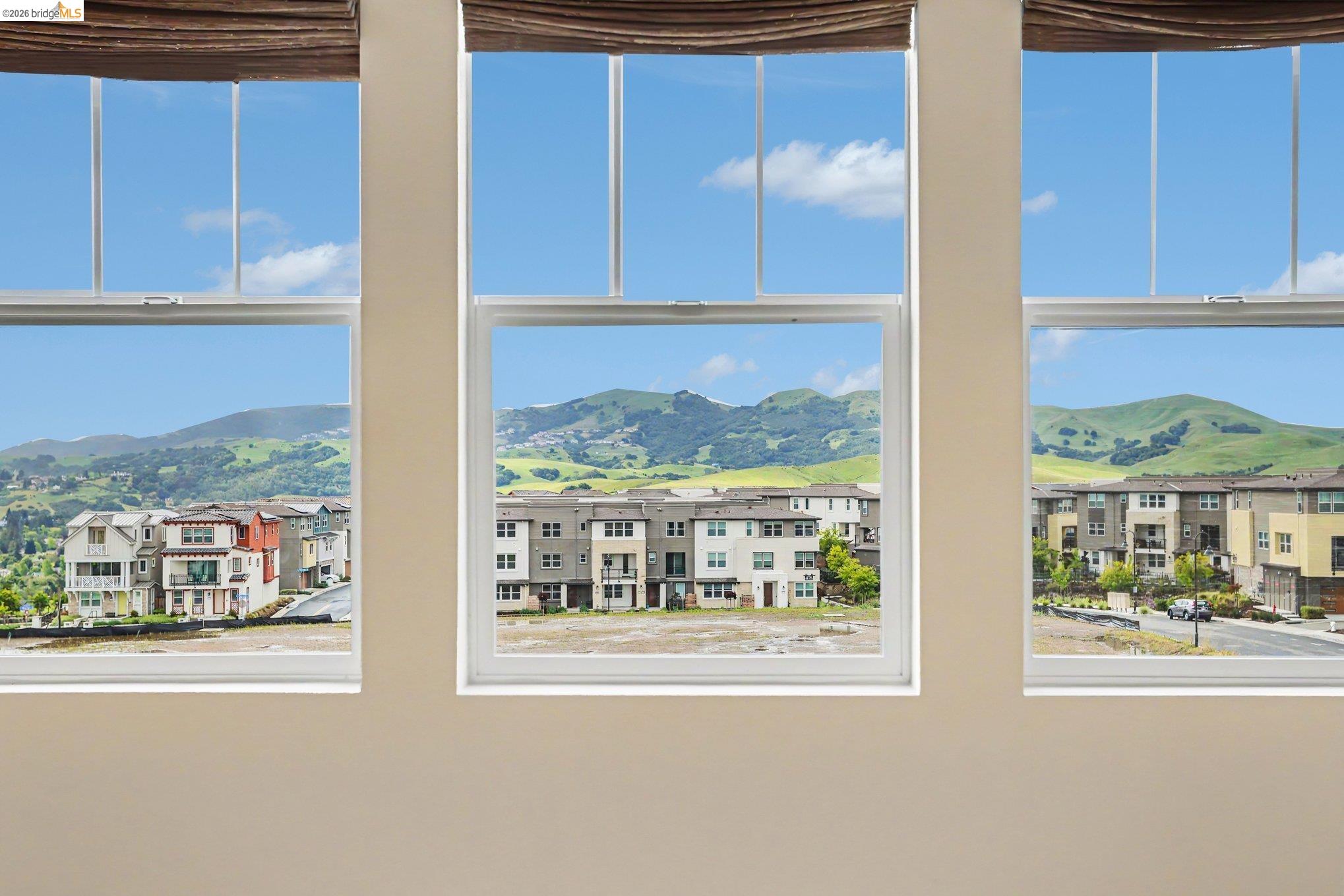 18210 Argento Loop San Ramon, CA 94583 - Photo 19 of 43 Three large windows with neutral-toned roller blinds offer expansive views of distant green hills and a residential neighborhood with varied architectural styles