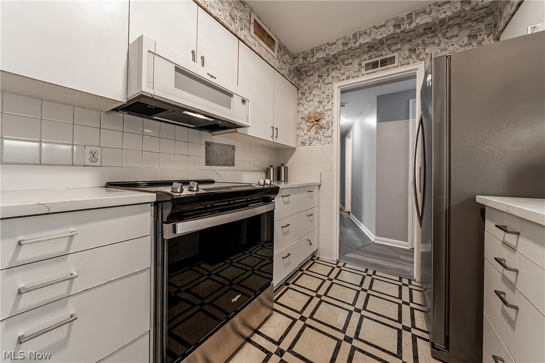 13800 Fairhill Road, Unit 306 Cleveland, OH 44120 - Photo 25 of 48 Kitchen with stainless steel appliances, white cabinetry, light countertops, wallpapered walls, and backsplash