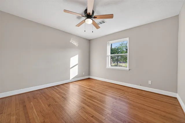 an empty room with wooden floor chandelier fan and windows
