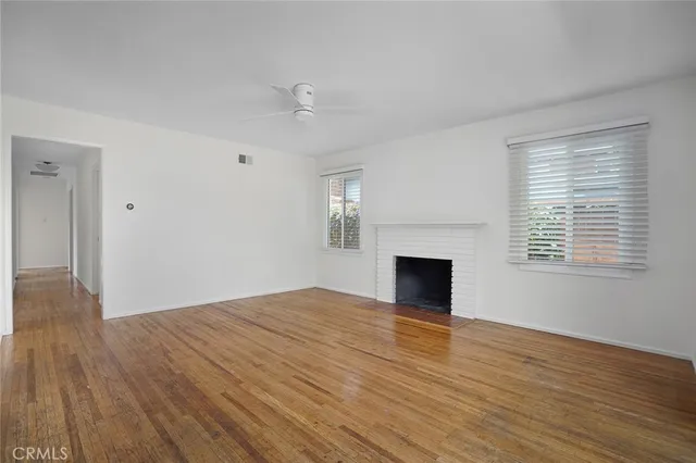 an empty room with wooden floor fireplace and windows