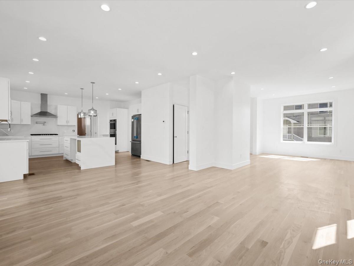 Contemporary kitchen with white cabinetry, stainless steel appliances, a center island with pendant lighting, and wood-finish flooring throughout