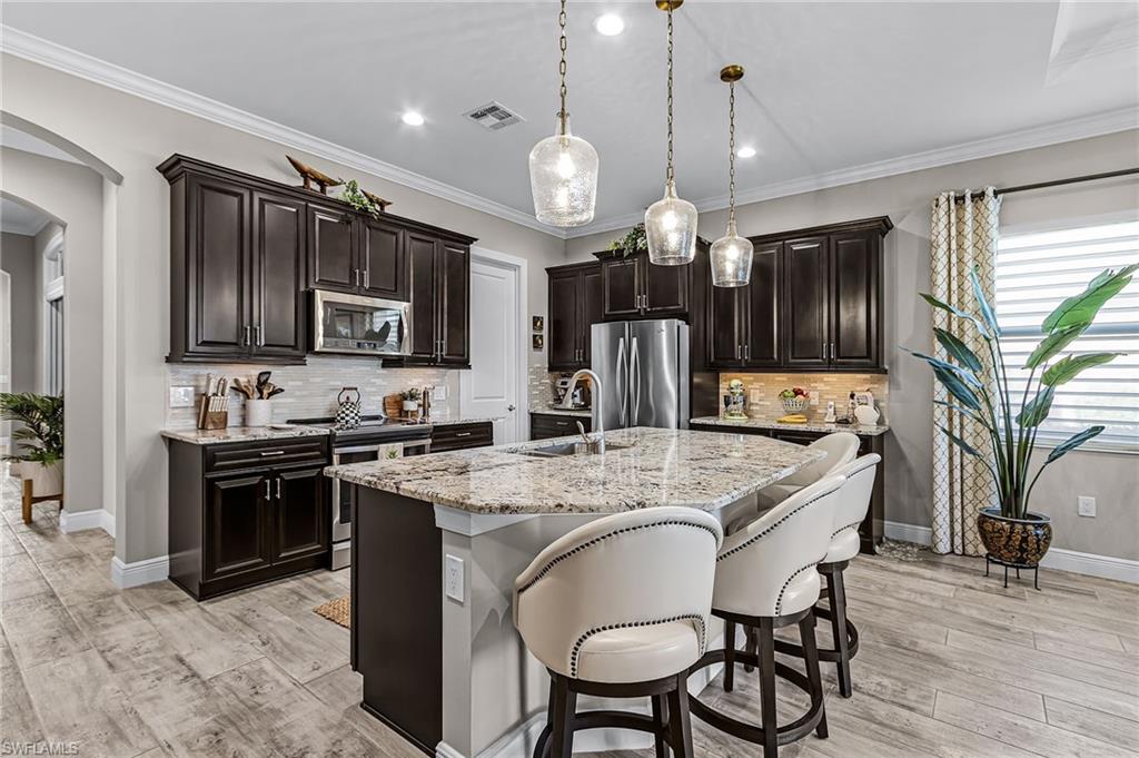 1434 Redona Way Naples, FL 34113 - Photo 23 of 47 a kitchen with stainless steel appliances granite countertop a stove a sink dishwasher a refrigerator a microwave oven with a dining table and chairs