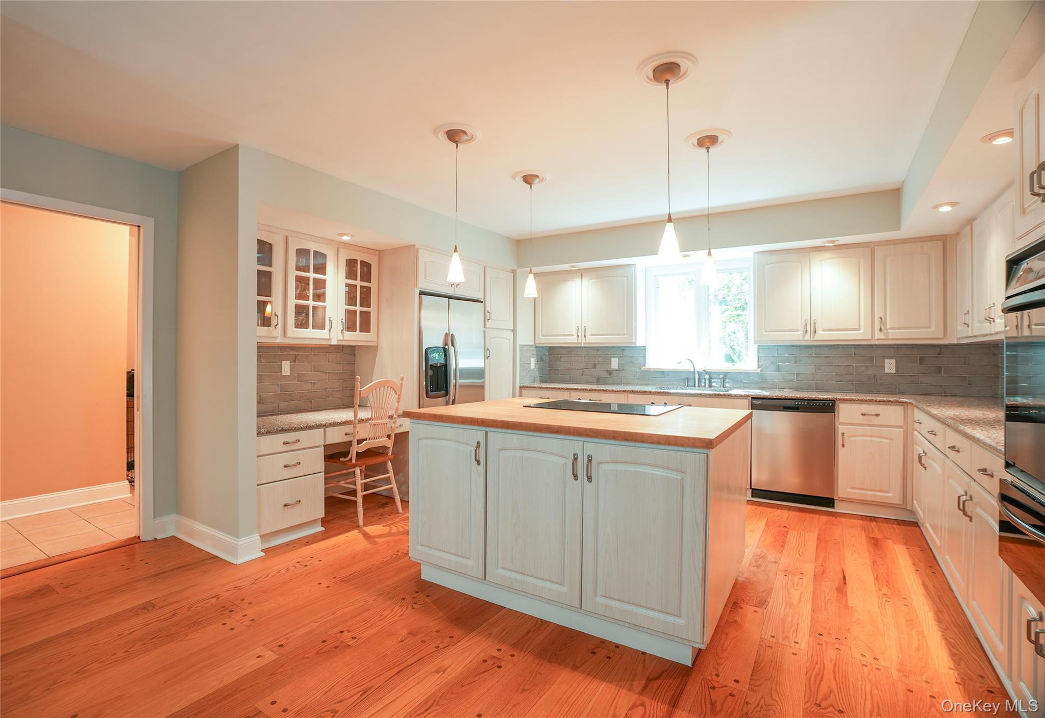 22 Peters Lane Pound Ridge, NY 10576 - Photo 11 of 43 Gourmet kitchen featuring wood-finish flooring, white cabinetry, an island with a wood countertop, stainless steel appliances, and a built-in desk area