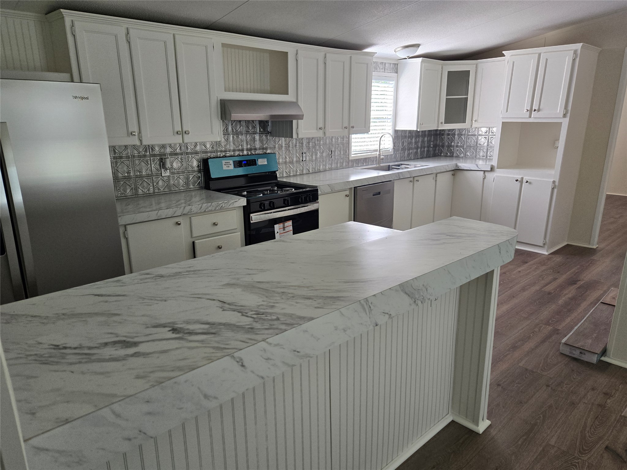 Kitchen featuring a breakfast bar with beadboard paneling, white cabinetry, stainless steel appliances, a tile backsplash, and wood-finish flooring