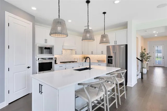 a kitchen with stainless steel appliances kitchen island granite countertop a dining table chairs and white cabinets