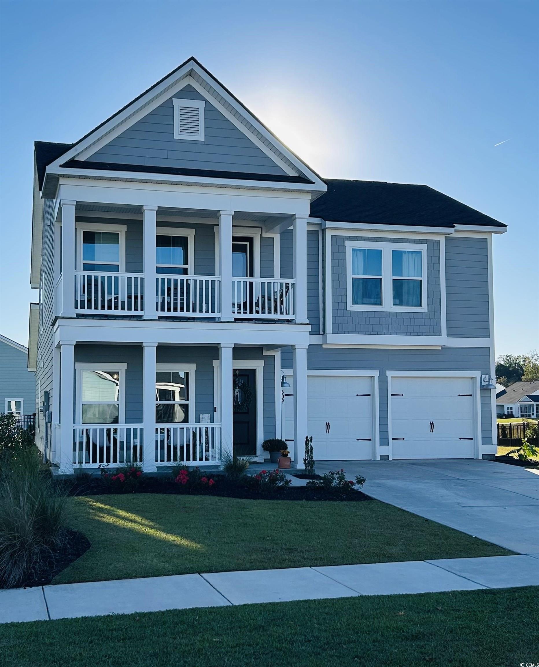 View of front facade with covered porch, driveway, a front yard, and an attached garage