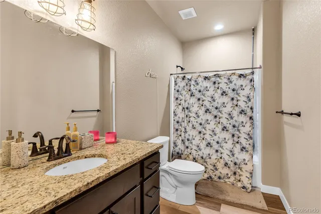 a bathroom with a granite countertop sink a toilet a mirror and shower curtain