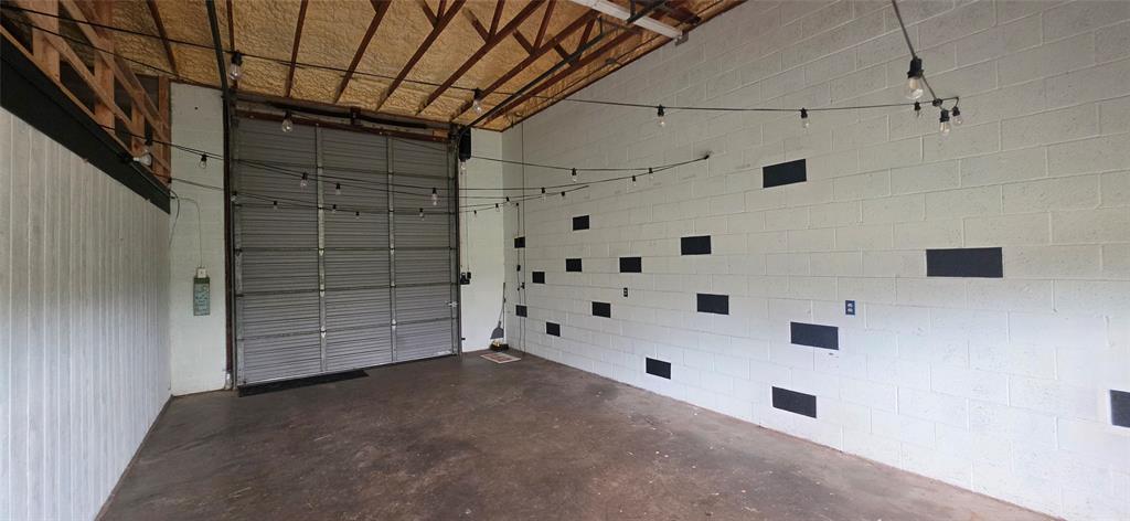 1214 Desvoignes Road Denison, TX 75021 - Photo 6 of 20 Concrete flooring, overhead garage door, exposed ceiling joists, string lighting, and painted block walls