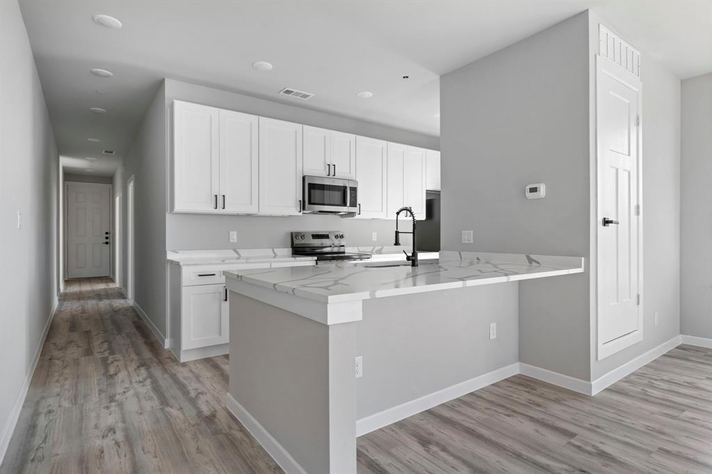 948 Corinth Street, Unit 13 Dallas, TX 75215 - Photo 8 of 18 Kitchen with white cabinetry, light stone countertops, stainless steel appliances, light wood-type flooring, and a peninsula