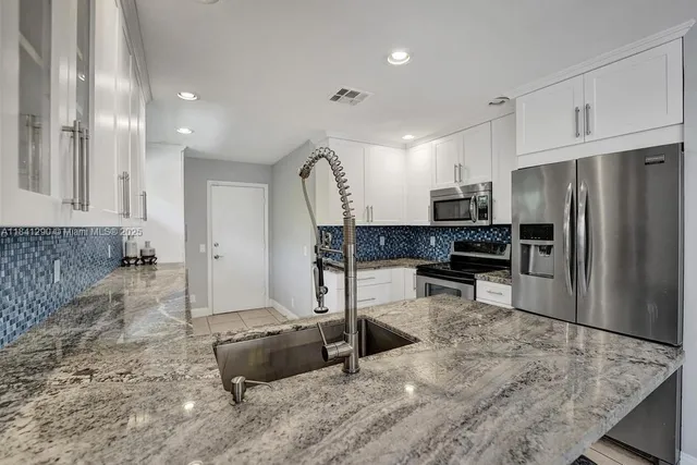 a kitchen with stainless steel appliances kitchen island granite countertop a refrigerator and a sink