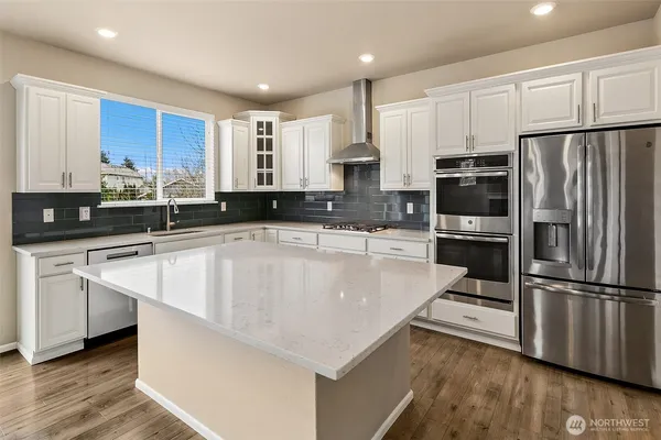 a kitchen with stainless steel appliances a stove a sink a refrigerator white cabinets and wooden floor