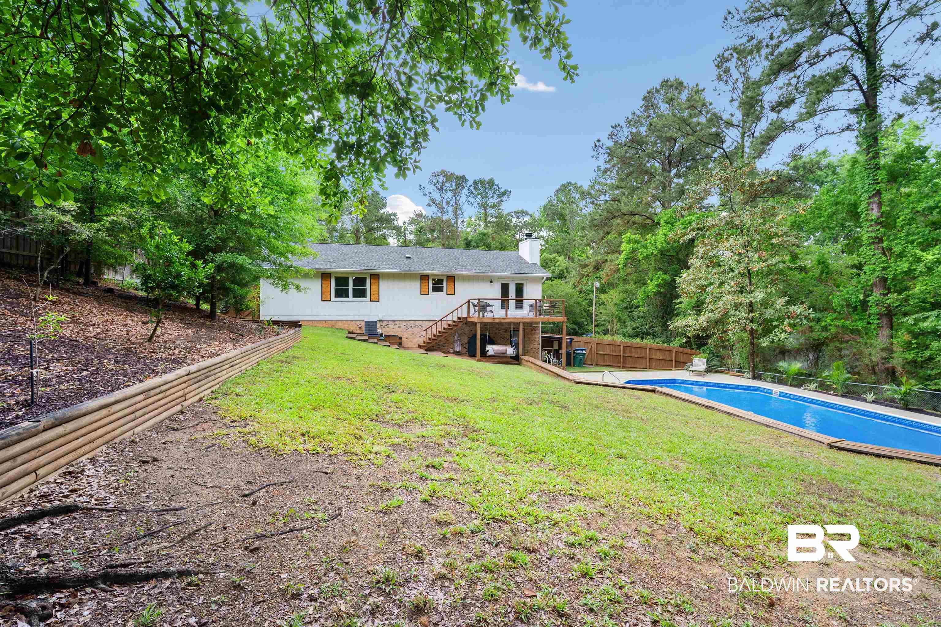 71 Caisson Trace Daphne, AL 36527 - Photo 31 of 36 Expansive backyard featuring a rectangular in-ground pool, a sloped lawn, a wooden retaining wall, and mature trees providing natural privacy