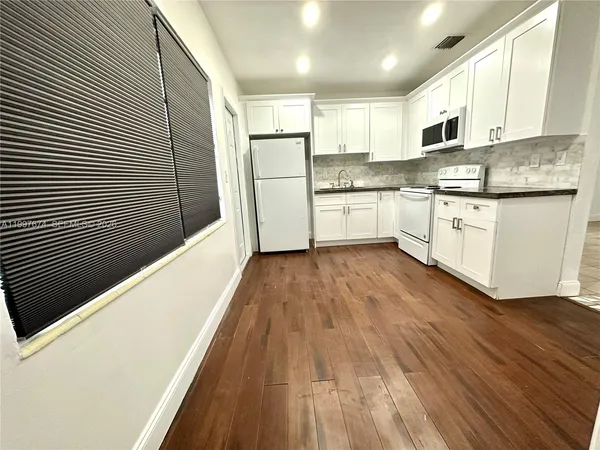 a kitchen with granite countertop wooden floors stainless steel appliances and white cabinets