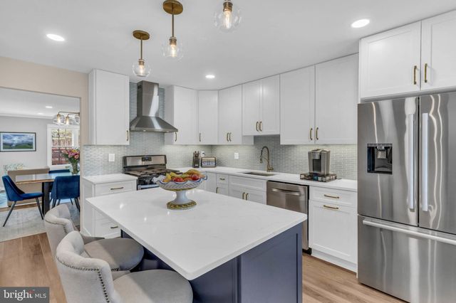 a kitchen with stainless steel appliances a stove a sink a refrigerator and chairs