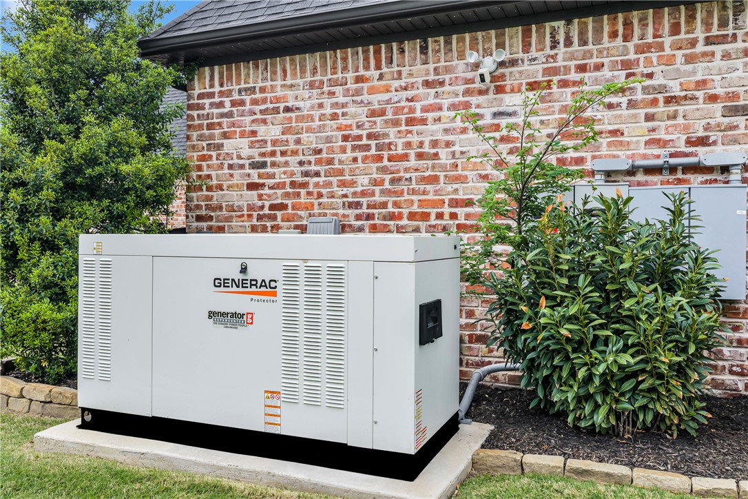 3510 Copper Ridge Road Rogers, AR 72756 - Photo 19 of 58 The property features a Generac Guardian Series whole home generator, situated on a concrete pad with a surrounding brick retaining wall, and mature landscaping