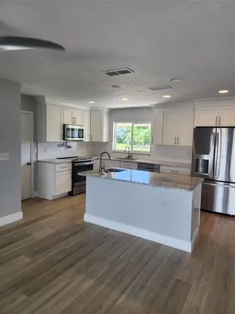 a living room with stainless steel appliances granite countertop a refrigerator a sink dishwasher a oven with white cabinets and wooden floor