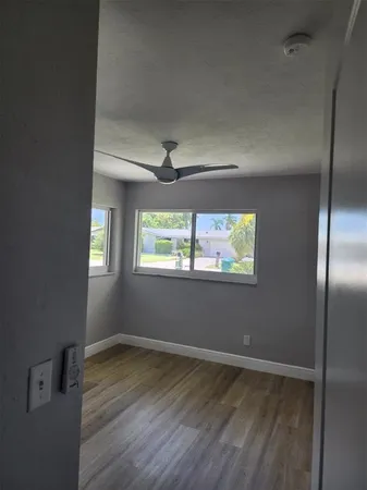 an empty room with wooden floor fan and windows
