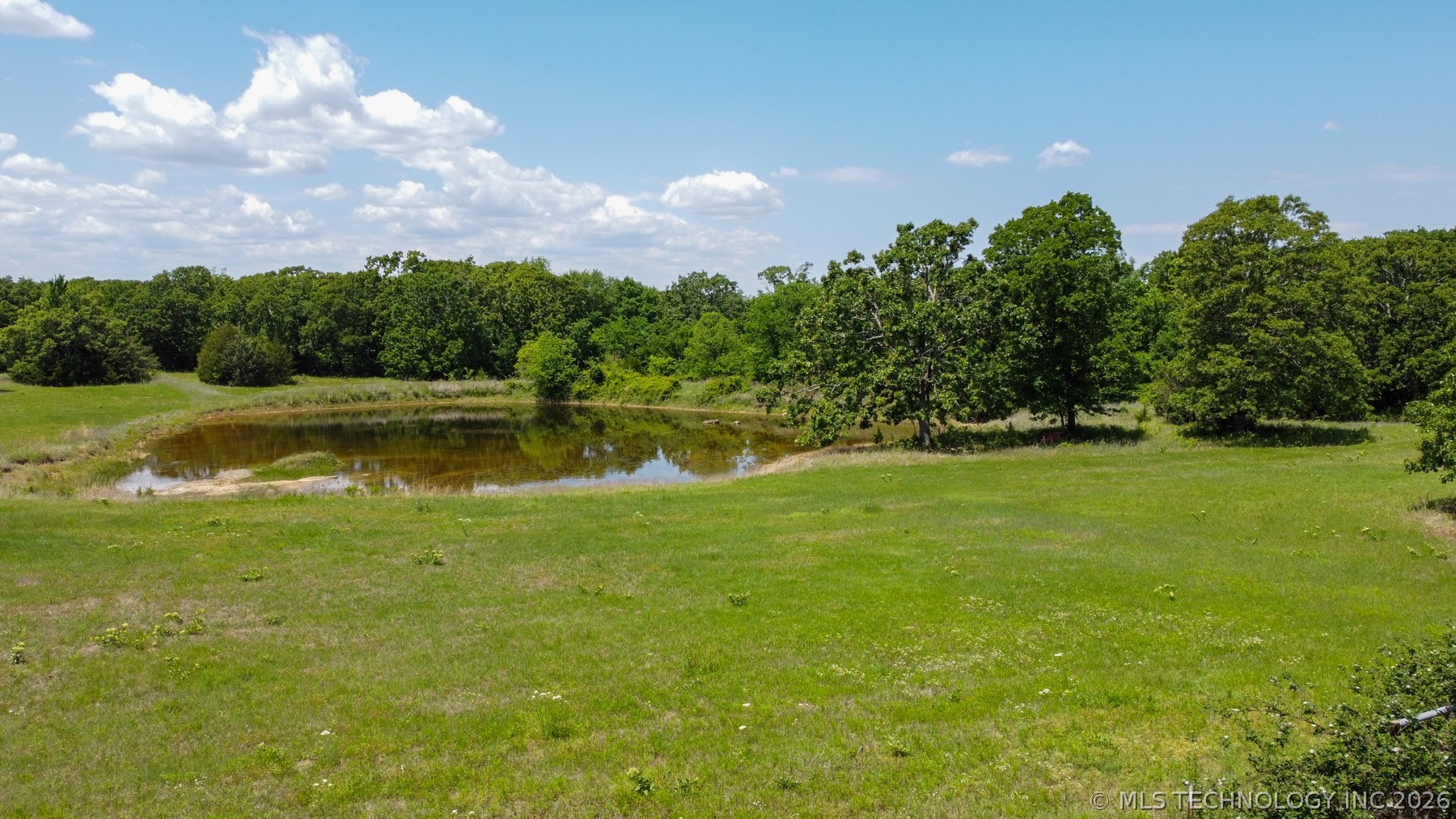 13248 North 3540th Road Maud, OK 74854 - Photo 18 of 98 Expansive green space featuring a tranquil pond, surrounded by mature trees and natural landscaping