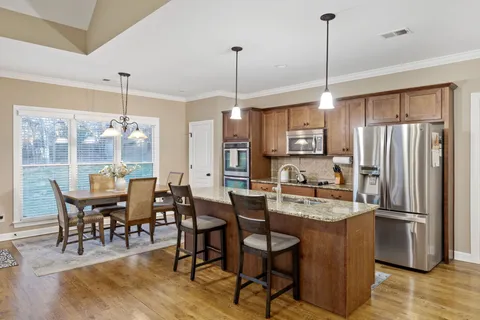 a kitchen with stainless steel appliances granite countertop a refrigerator a kitchen island a dining table and chairs