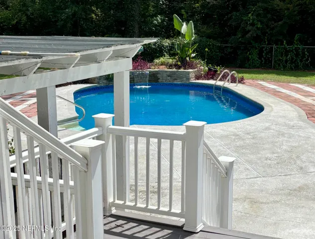 a view of swimming pool with seating space and trees in the background