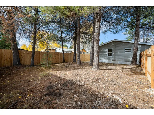 a backyard of a house with large trees and wooden fence