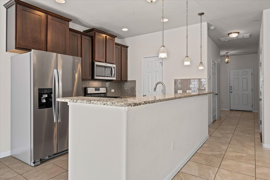1609 Catalan Road, Unit 1802 Austin, TX 78748 - Photo 7 of 25 Kitchen with stainless steel appliances, dark brown cabinets, decorative backsplash, light stone countertops, and recessed lighting