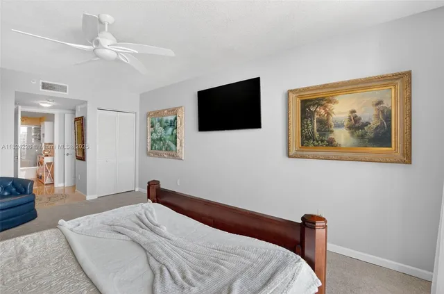 a bedroom with a large bed a flat tv screen and a ceiling fan