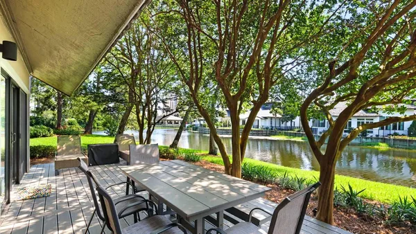 a view of a patio with table and chairs next to a yard with large trees