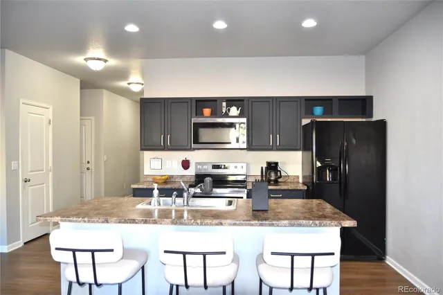 a kitchen with stainless steel appliances granite countertop a dining table chairs refrigerator and sink