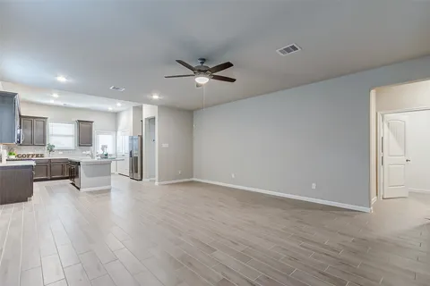 a view of an empty room and kitchen view with wooden floor
