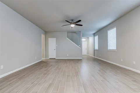 an empty room with wooden floor ceiling fan and windows