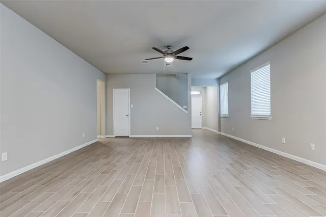 an empty room with wooden floor ceiling fan and windows