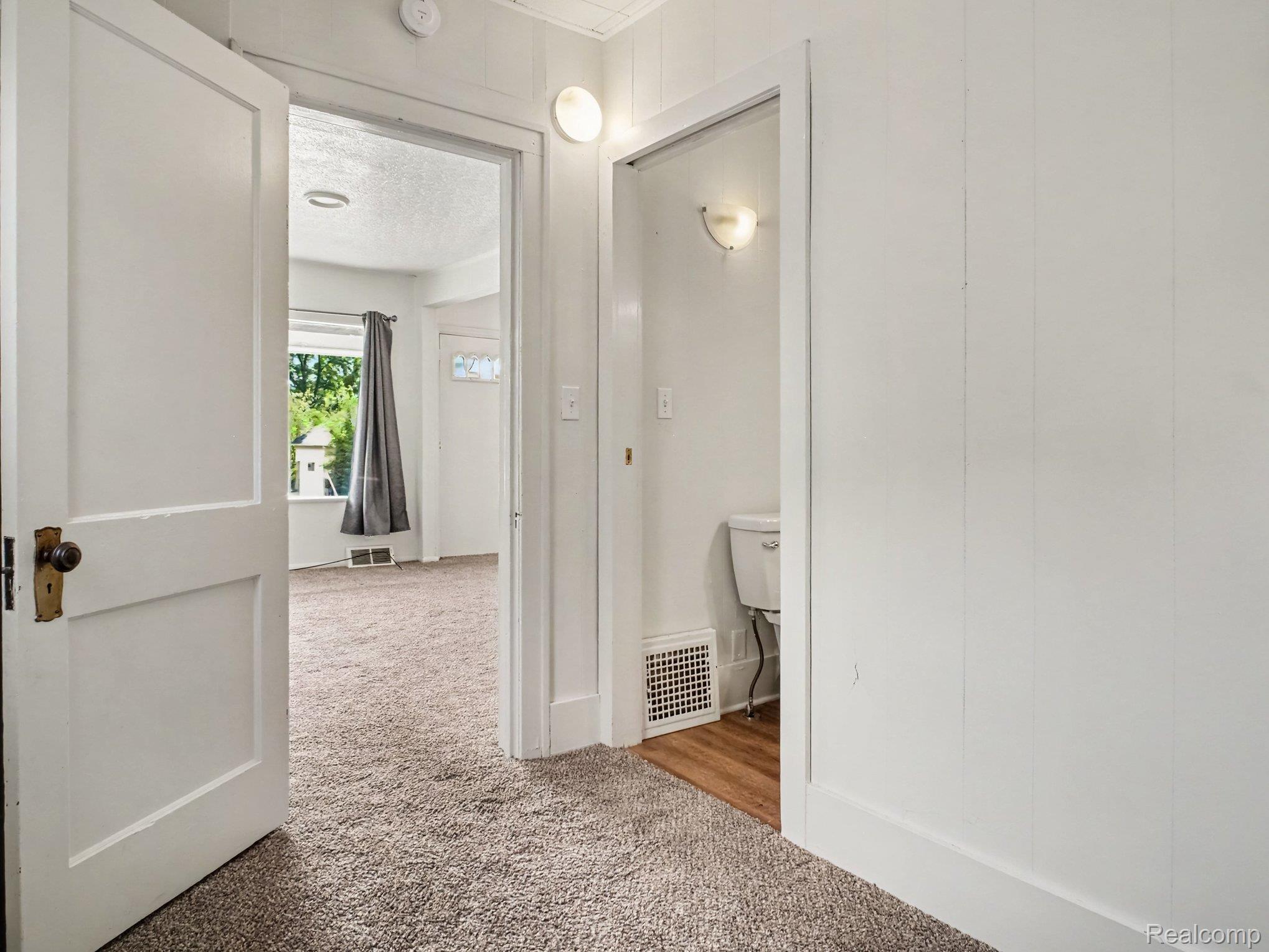 2840 Miller Road Flint, MI 48503 - Photo 19 of 49 Carpeted hallway with white panel walls, leading to a room with a window and a separate area featuring wood-finish flooring