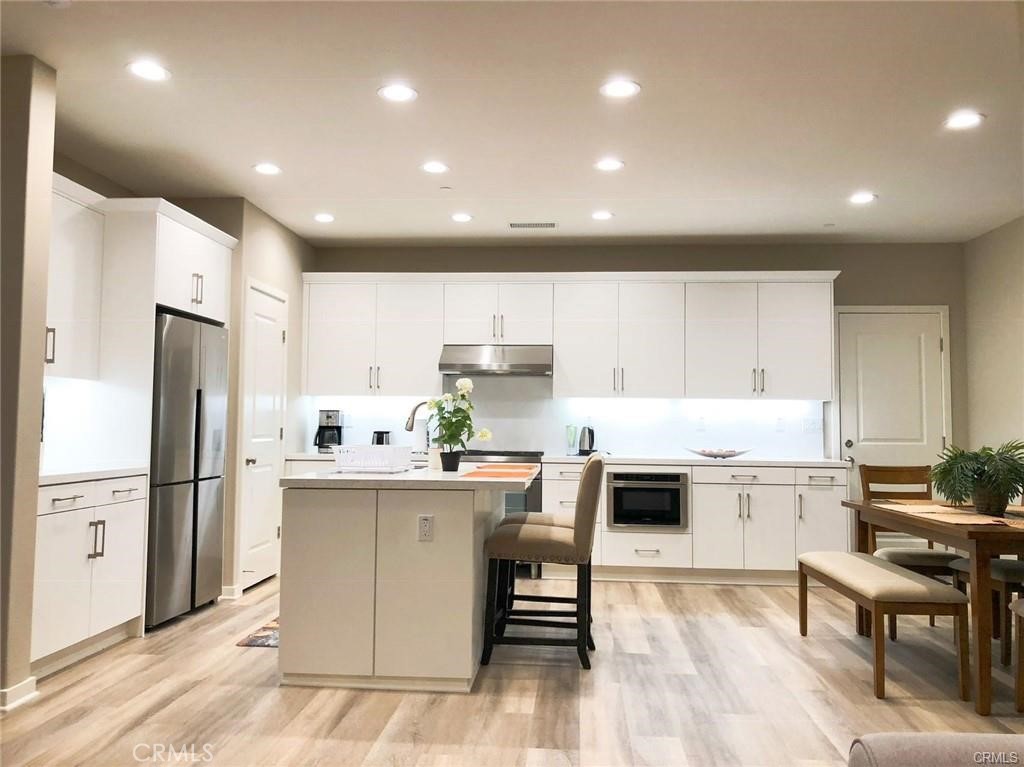 a kitchen with stainless steel appliances kitchen island granite countertop a refrigerator oven a sink dishwasher and a dining table with wooden floor