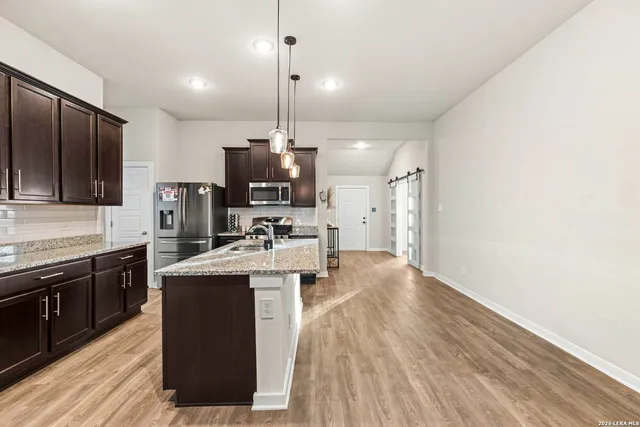 a kitchen with stainless steel appliances kitchen island granite countertop a sink a stove and a wooden floors