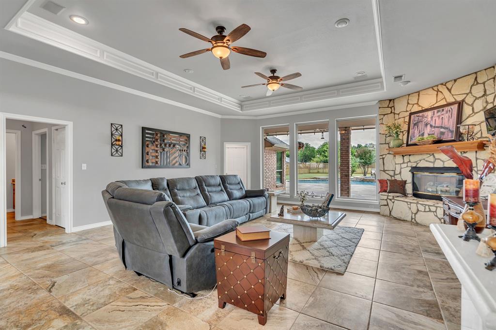 50 Buckingham Lane Allen, TX 75002 - Photo 16 of 39 Living area featuring a raised ceiling, a ceiling fan, ornamental molding, a stone fireplace, and recessed lighting