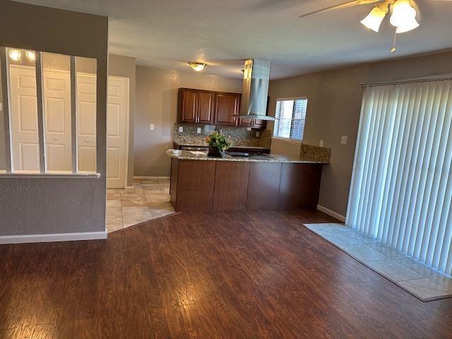 Kitchen featuring light wood finished floors, tasteful backsplash, dark stone counters, a peninsula, and range hood