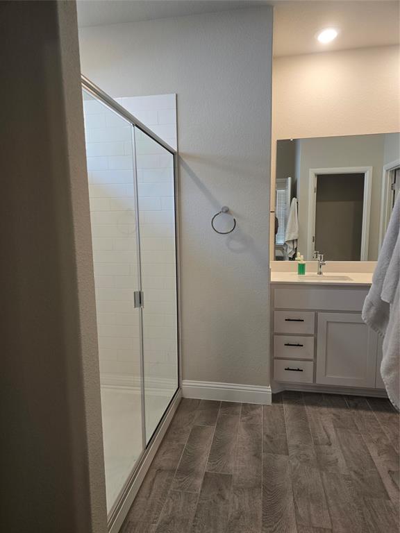 1704 Razorbill Road Denton, TX 76205 - Photo 10 of 20 Contemporary bathroom featuring a glass-enclosed shower with subway tile surround, wood-finish flooring, a single vanity with a white countertop, and a large mirror