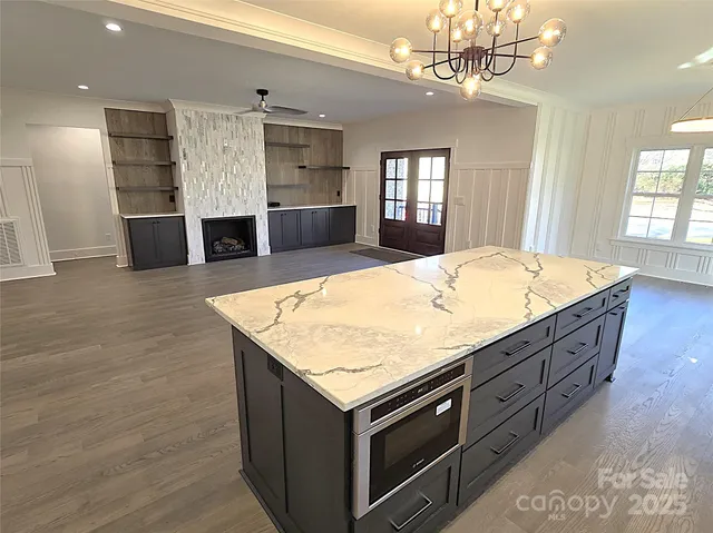 a room with kitchen island a sink stainless steel appliances living room and fireplace