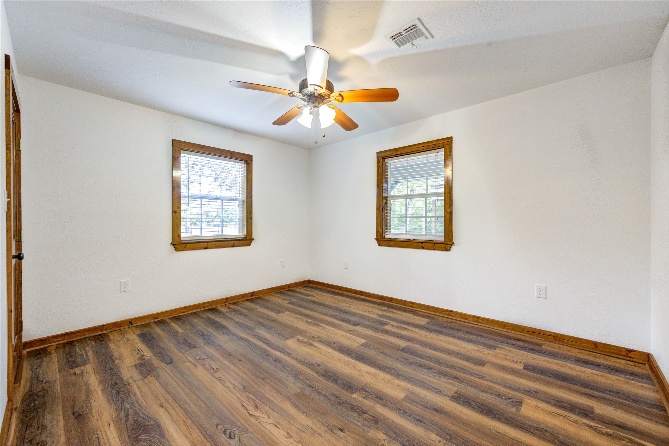 8805 Sun Oil Road Brenham, TX 77833 - Photo 33 of 50 Bright and inviting bedroom featuring rich wood flooring, two large windows with natural wood trim, and a stylish ceiling fan for added comfort.
