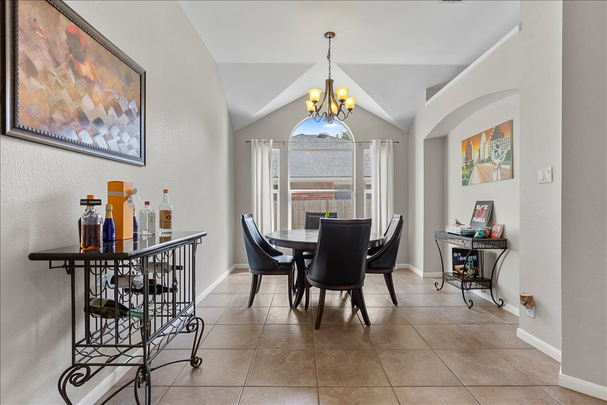 9012 Meacham Way Austin, TX 78749 - Photo 7 of 34 Vaulted ceiling dining area featuring a prominent arched window, tiled flooring, an elegant chandelier, and an arched entryway