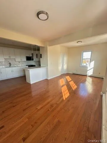 a view of kitchen and empty room with wooden floor