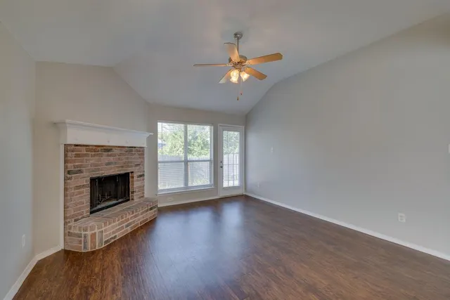 a view of an empty room with wooden floor and a fireplace