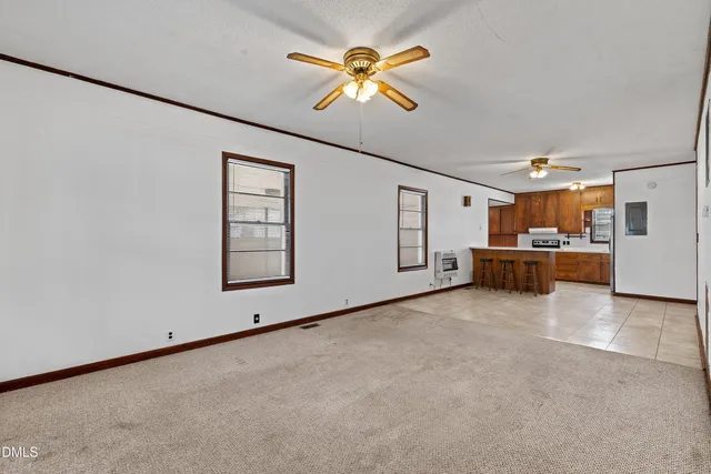 a view of an empty room with a ceiling fan and kitchen view