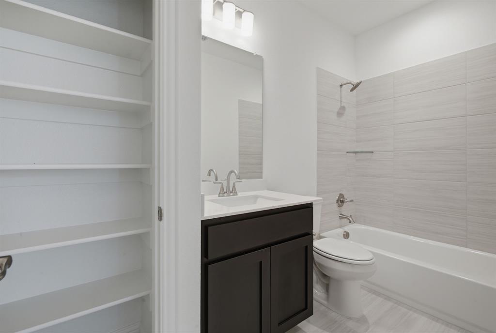 2911 Hanscom Street Forney, TX 75126 - Photo 34 of 40 Full-height shelving unit, dark wood-finish vanity with white countertop, integrated sink with brushed nickel faucet, light gray tiled bathtub surround, and light wood-finish flooring