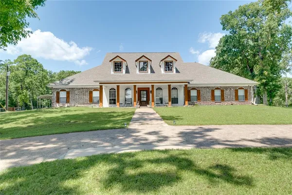 a view of house in front of a big yard with large trees