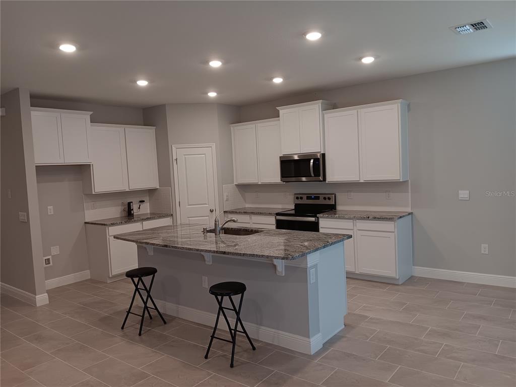 5433 Southwest 44th Ct Road Ocala, FL 34474 - Photo 3 of 24 a kitchen with a sink a microwave a stove a refrigerator and white cabinets with wooden floor